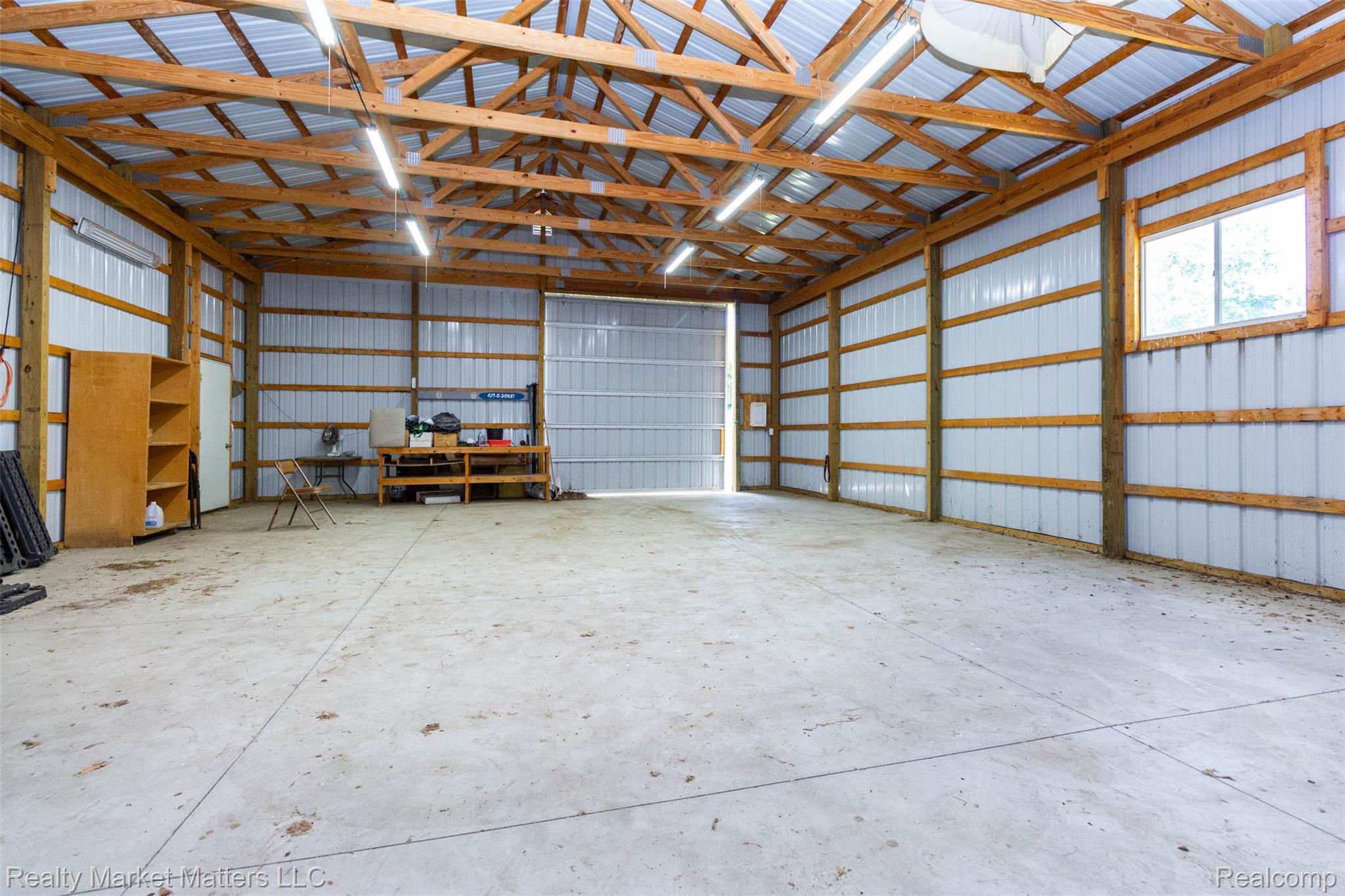 4951 Laur Road North Branch, MI 48461 - Photo 28 of 34 Spacious utility building featuring a concrete slab floor, exposed wood beam ceiling, metal siding, multiple windows, and a large roll-up door
