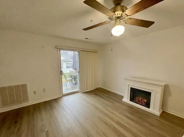an empty room with wooden floor a ceiling fan a fireplace and windows