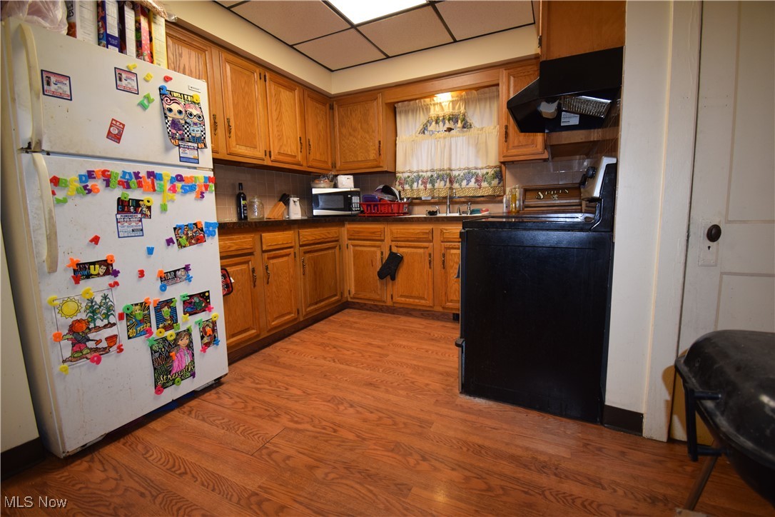 913 Lawrence Road Northeast Canton, OH 44704 - Photo 6 of 10 Kitchen featuring dark countertops, stove, freestanding refrigerator, light wood-type flooring, and exhaust hood