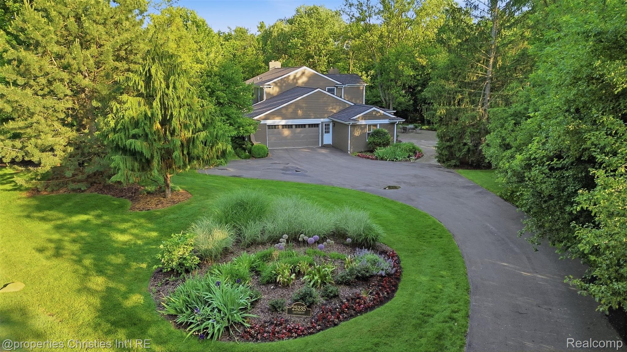 25235 Canterbury Road Franklin, MI 48025 - Photo 45 of 56 Gable-roof property featuring a wide driveway, mature trees, manicured lawns, a circular garden bed, and an attached garage.
