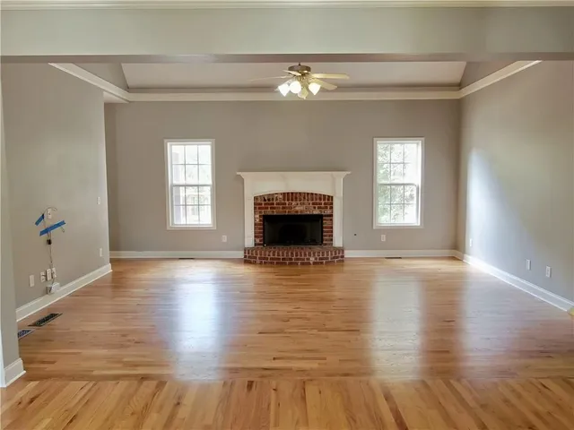 an empty room with wooden floor fireplace and windows
