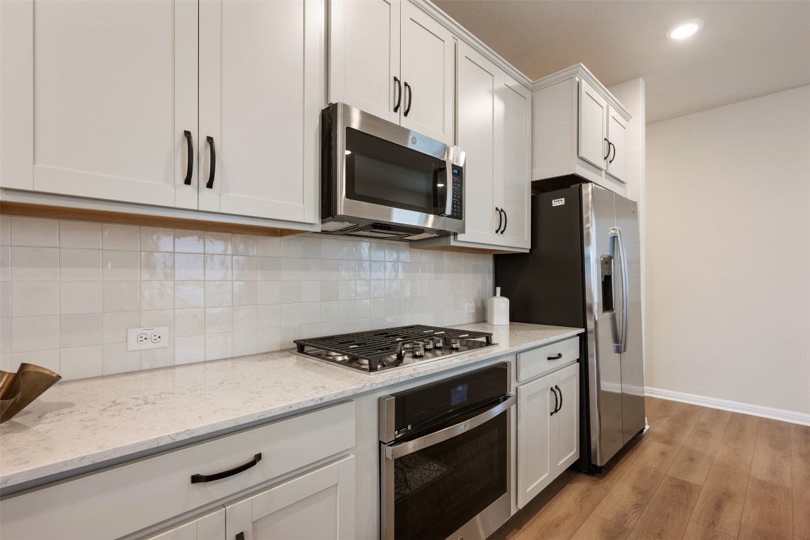 283 Ranier Way Dripping Springs, TX 78620 - Photo 10 of 39 Kitchen featuring stainless steel appliances, light stone countertops, white cabinetry, light wood-type flooring, and decorative backsplash
