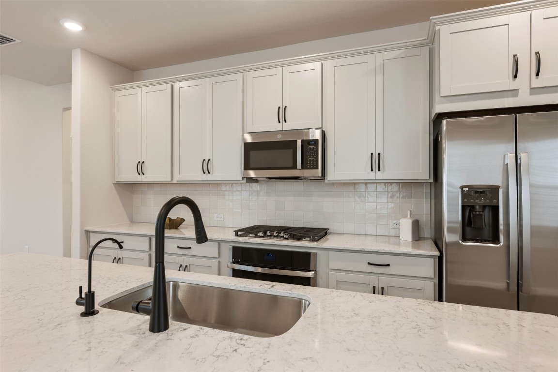 283 Ranier Way Dripping Springs, TX 78620 - Photo 11 of 39 Kitchen with stainless steel appliances, tasteful backsplash, white cabinets, light stone counters, and recessed lighting