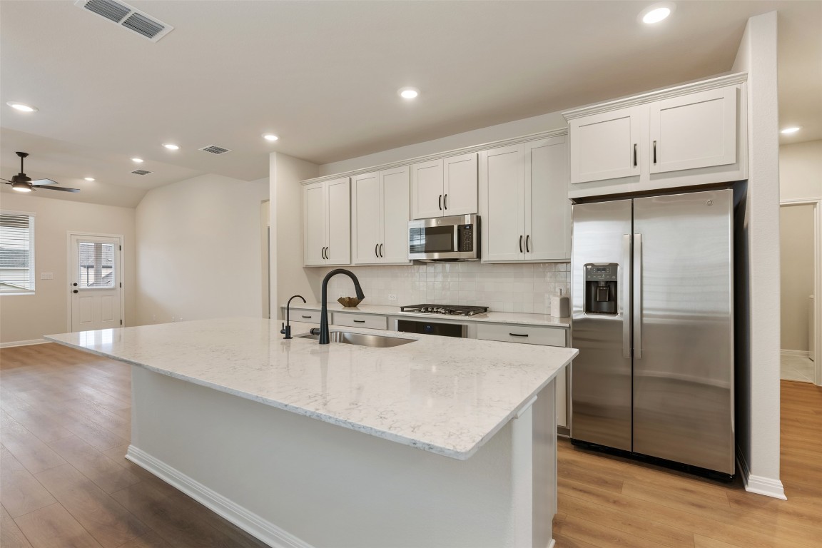 283 Ranier Way Dripping Springs, TX 78620 - Photo 6 of 39 Kitchen with stainless steel appliances, light stone counters, tasteful backsplash, white cabinetry, and an island with sink