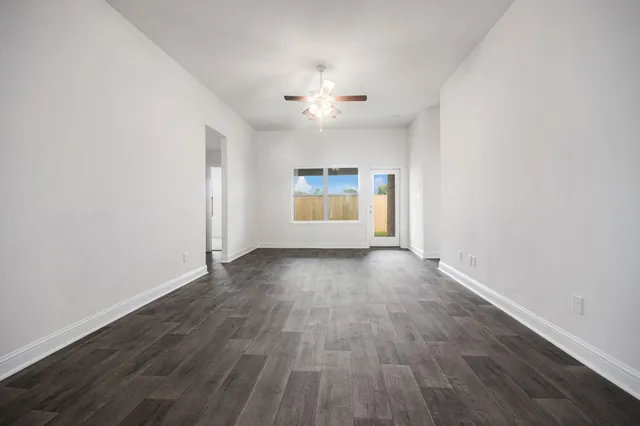 an empty room with wooden floor chandelier fan and windows
