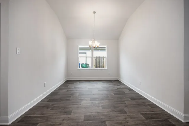 an empty room with wooden floor chandelier and windows