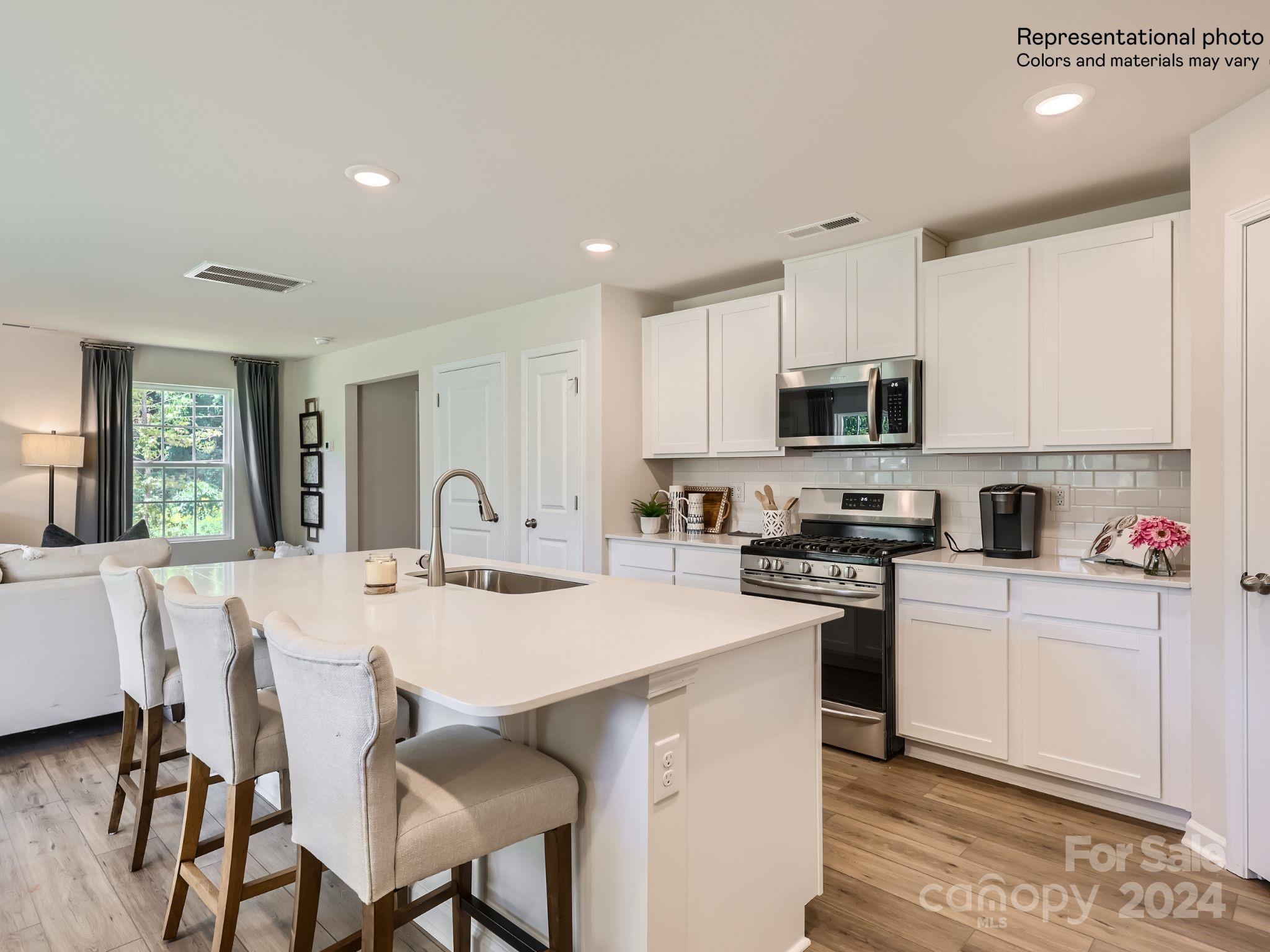 15237 Windy Plns Road Charlotte, NC 28262 - Photo 3 of 24 a kitchen with stainless steel appliances granite countertop a stove a sink a microwave a refrigerator with white cabinets and wooden floor