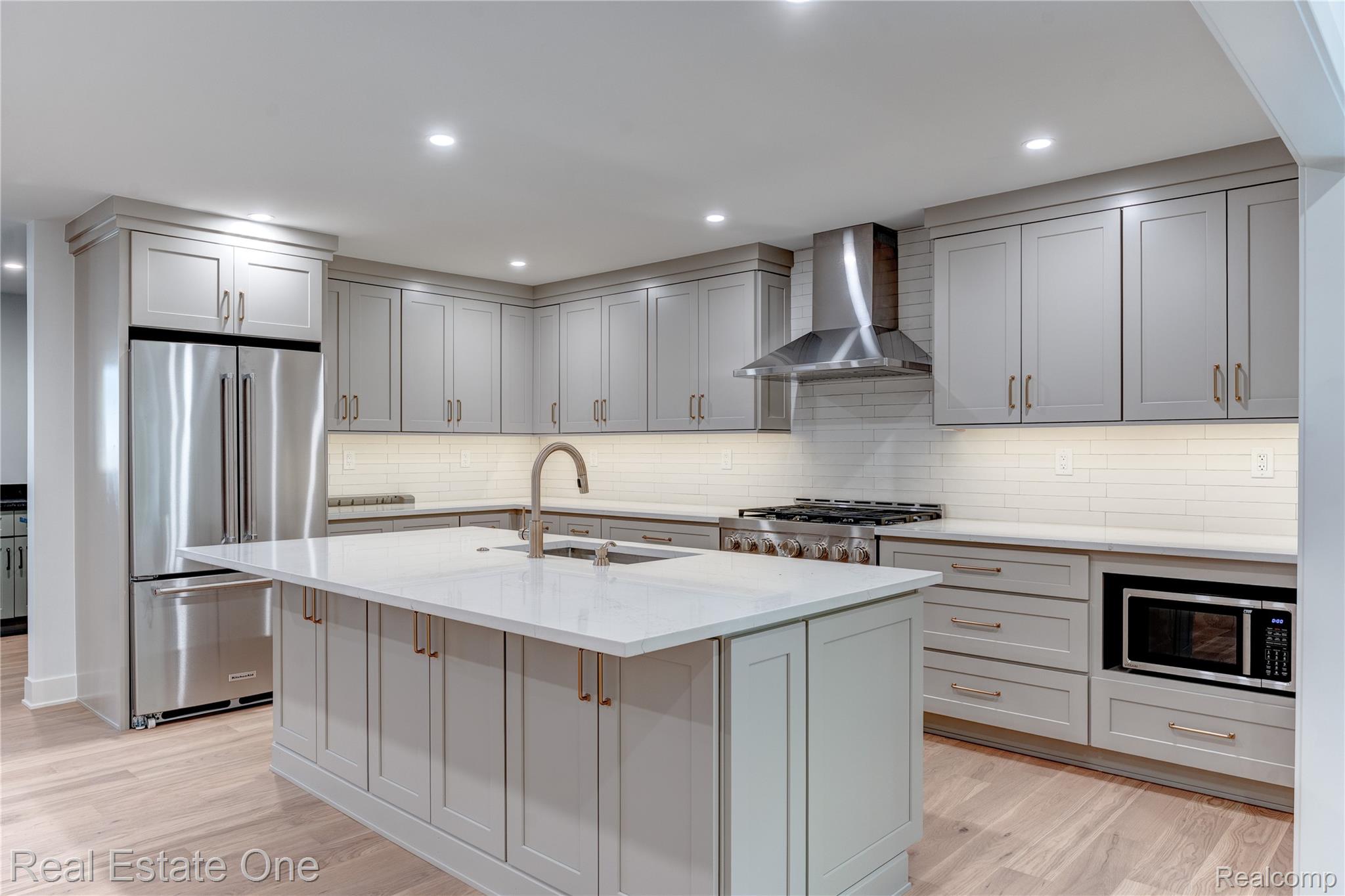 786 South Cranbrook Road Bloomfield Hills, MI 48301 - Photo 7 of 38 Kitchen with stainless steel appliances, light stone countertops, wall chimney range hood, light wood-type flooring, and decorative backsplash