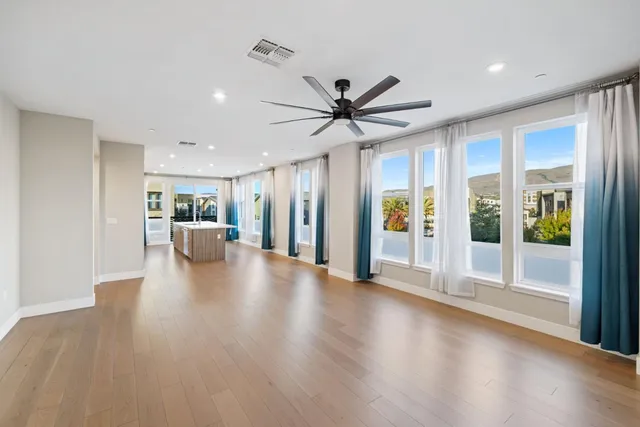 a view of a big room with wooden floor a ceiling fan and windows