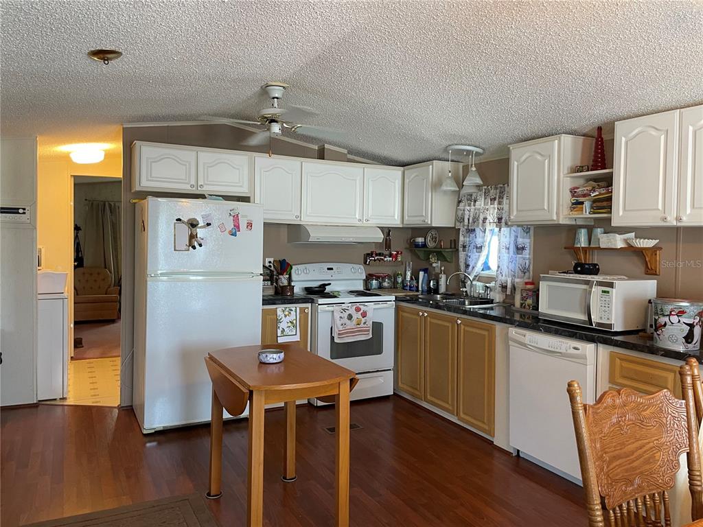 251 Patterson Road, Unit C31 Haines City, FL 33844 - Photo 8 of 16 a kitchen with granite countertop a refrigerator a stove a sink dishwasher and white cabinets with wooden floor
