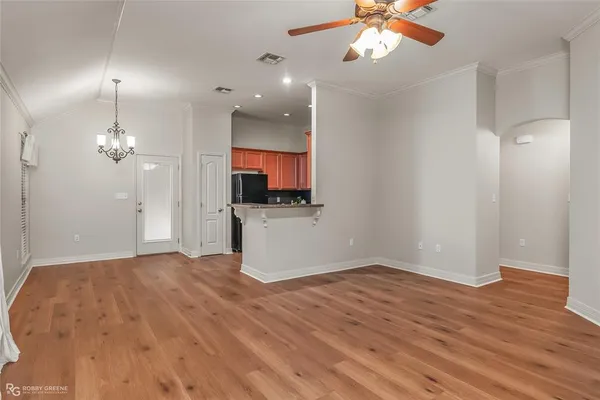 a view of empty room with wooden floor and kitchen