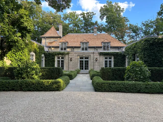 a view of a white house with a yard plants and large tree