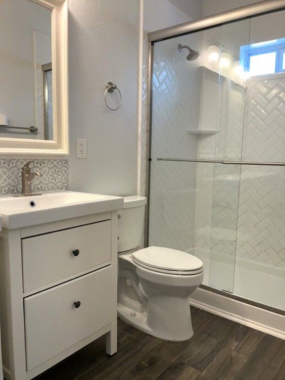 806 East 3rd Street Georgetown, TX 78626 - Photo 8 of 16 Bathroom featuring vanity, a shower stall, dark wood finished floors, backsplash, and a textured wall
