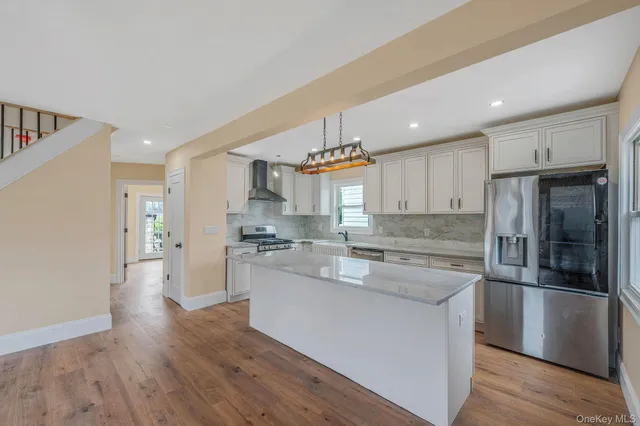 a kitchen with stainless steel appliances granite countertop a refrigerator a sink dishwasher a stove and white countertops with wooden floor