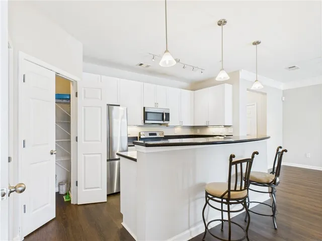 a kitchen with stainless steel appliances a stove a refrigerator a sink and white cabinets with wooden floor