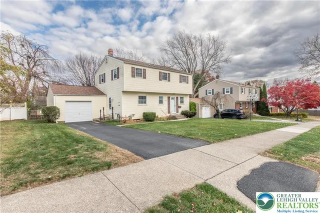 a view of a white house next to a yard with big trees