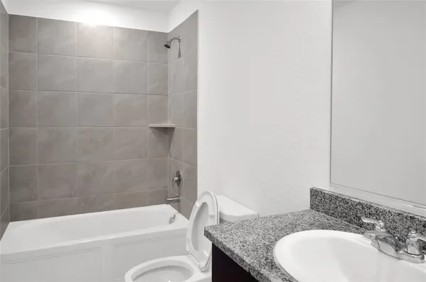 a bathroom with a granite countertop bathtub shower sink vanity and toilet