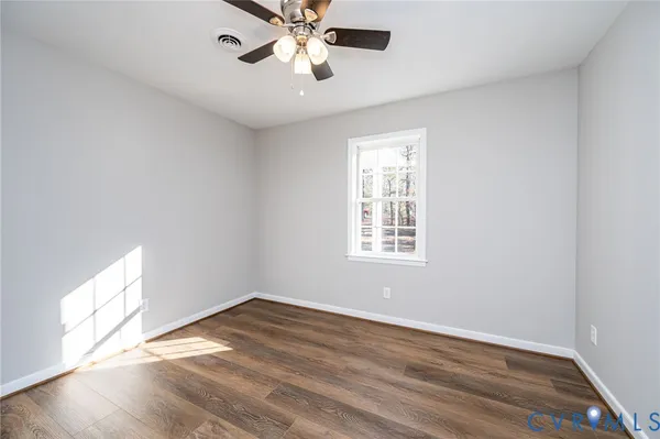 an empty room with wooden floor chandelier fan and windows