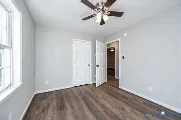 an empty room with wooden floor chandelier fan and windows