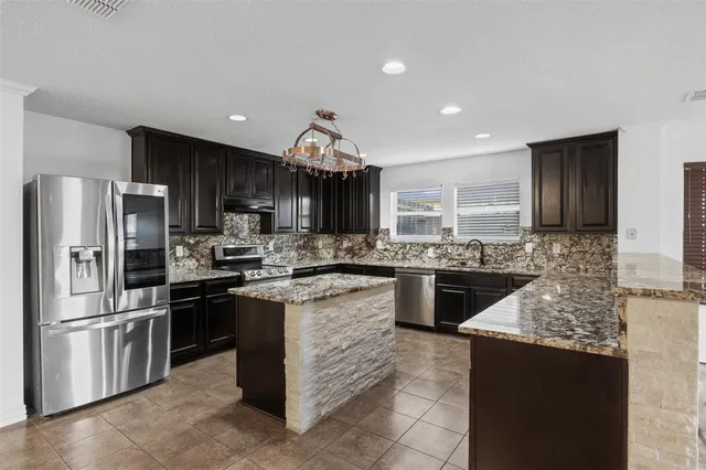 a kitchen with stainless steel appliances granite countertop a stove top oven a sink and a refrigerator