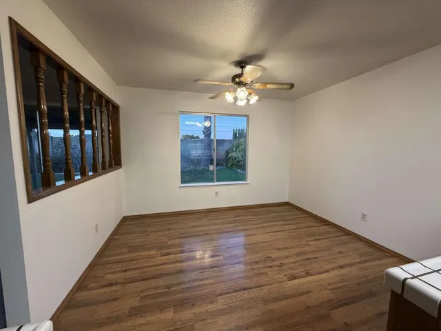 a view of an empty room with window chandelier fan and wooden floor