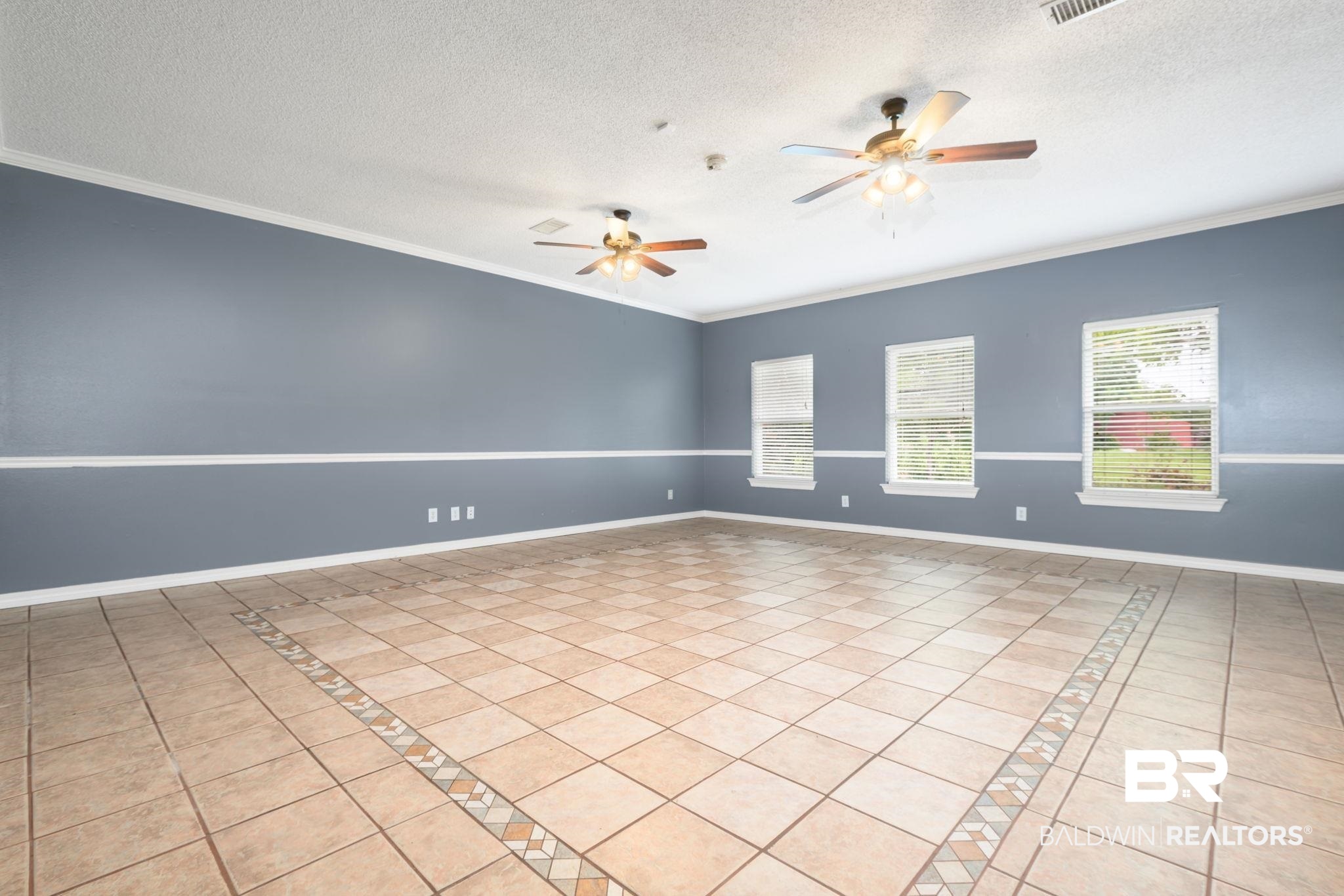 7540 2 Mile Road Irvington, AL 36544 - Photo 27 of 82 Spacious room featuring neutral-toned tile flooring with decorative inlay, two ceiling fans, and three windows providing natural light
