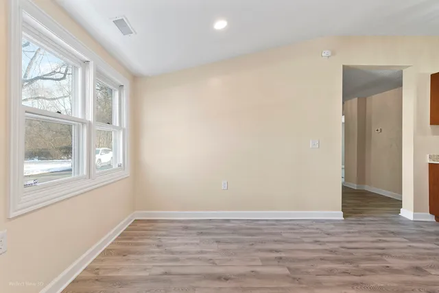 a view of an empty room with wooden floor and a window