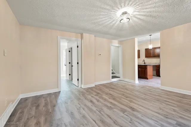 a view of empty room with wooden floor and kitchen view