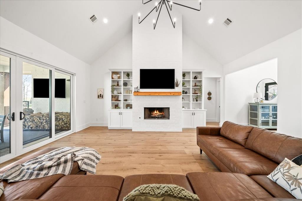 4363 Serenity Trail McKinney, TX 75071 - Photo 1 of 1 Living room featuring light wood finished floors, visible vents, a lit fireplace, and an inviting chandelier
