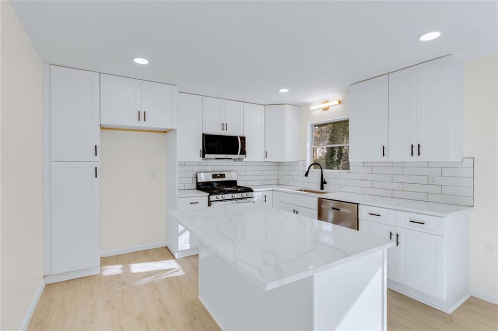6695 Cedar Hurst Trail Atlanta, GA 30349 - Photo 6 of 24 a large white kitchen with a stove a sink a refrigerator and white cabinets with wooden floor