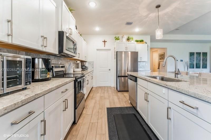 16033 Southwest 277th Street Homestead, FL 33031 - Photo 10 of 37 a large kitchen with stainless steel appliances kitchen island granite countertop a refrigerator a stove a sink dishwasher and white cabinets with wooden floor