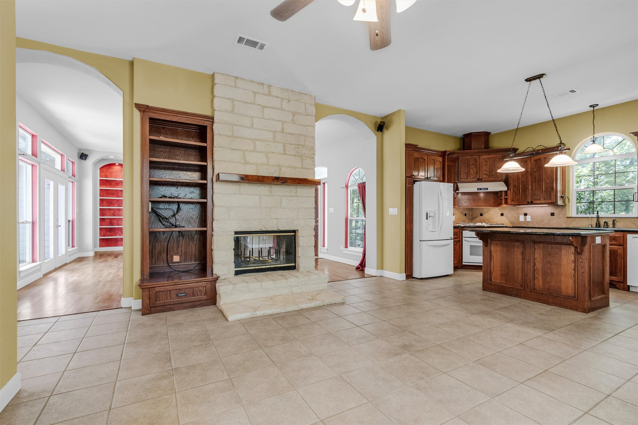 10331 Iron Ore Road Conroe, TX 77303 - Photo 8 of 47 Spacious open-concept featuring a charming stone fireplace, elegant built-in shelving, and a modern kitchen with rich wood cabinetry and an island. Bright natural light fills the space through arched windows, creating a warm and inviting atmosphere.