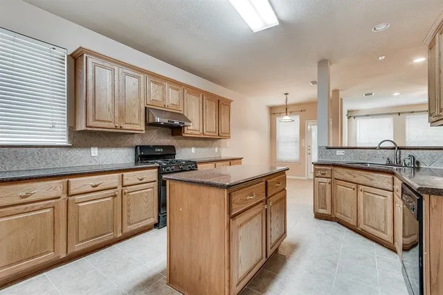 a kitchen with stainless steel appliances granite countertop a stove top oven a sink dishwasher and a refrigerator with wooden cabinets