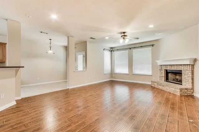 an empty room with wooden floor a ceiling fan a fireplace and windows