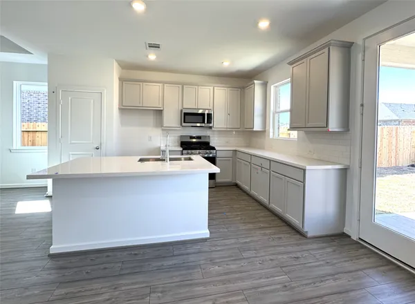 a large kitchen with stainless steel appliances granite countertop a stove a sink dishwasher and a large refrigerator with wooden floor