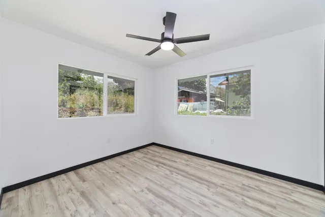 an empty room with wooden floor chandelier fan and windows