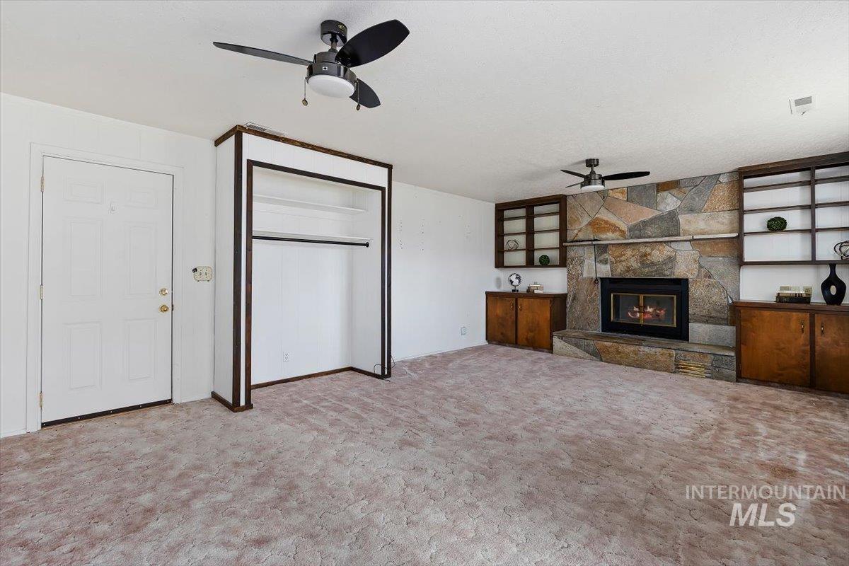 1214 H Street Rupert, ID 83350 - Photo 17 of 35 Unfurnished living room featuring a ceiling fan, a stone fireplace, carpet floors, and a textured ceiling