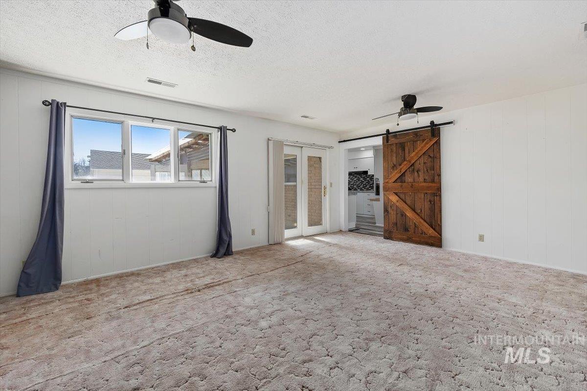 1214 H Street Rupert, ID 83350 - Photo 21 of 35 Spare room with a ceiling fan, a barn door, wood walls, a textured ceiling, and carpet