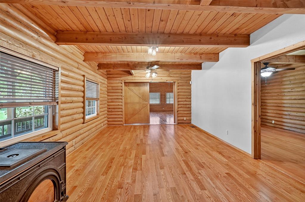 570 Ayres Road Bells, TX 75414 - Photo 15 of 39 Unfurnished living room with ceiling fan, rustic walls, light wood-style floors, and a wooden ceiling with exposed beams