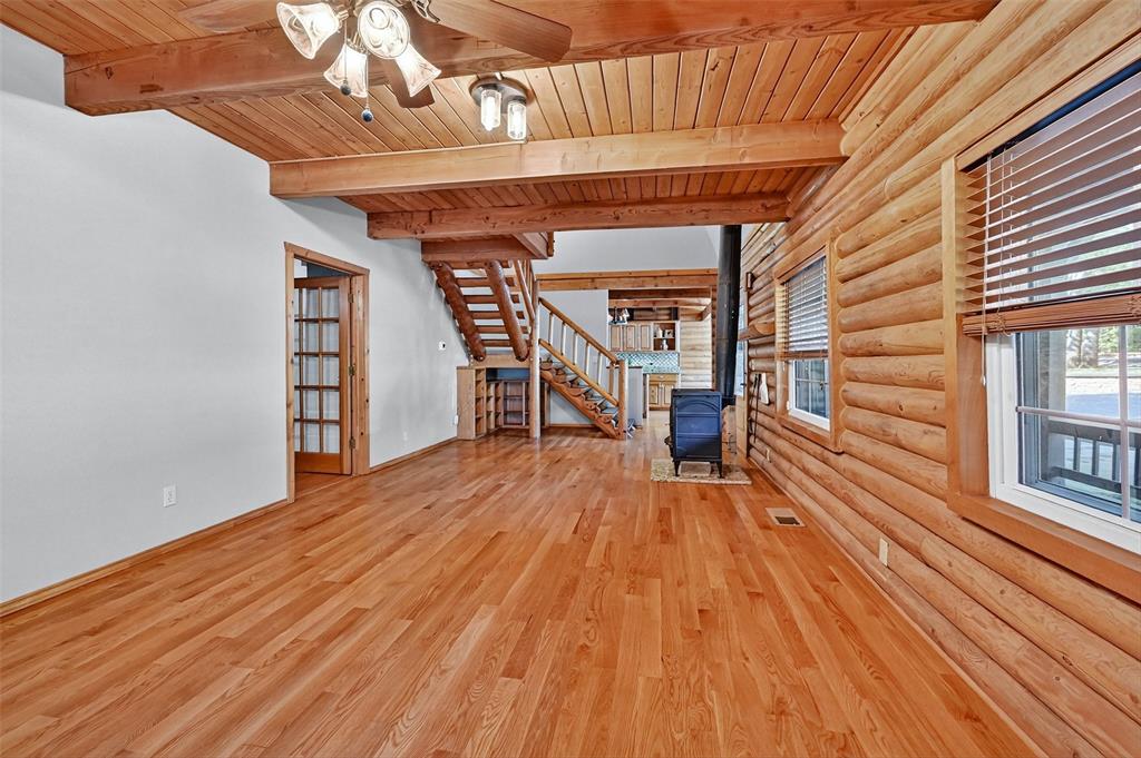 570 Ayres Road Bells, TX 75414 - Photo 8 of 39 Unfurnished living room with log walls, a wood stove, a wood ceiling with exposed beams, wood finished floors, and ceiling fan