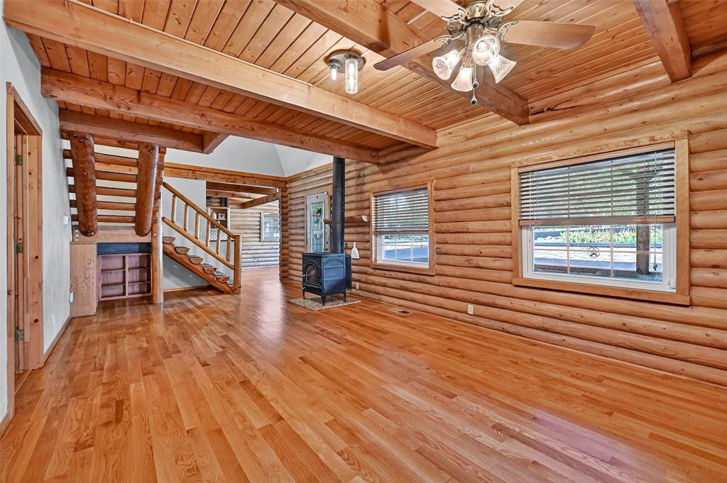 570 Ayres Road Bells, TX 75414 - Photo 9 of 39 Unfurnished living room with a wood stove, a wooden ceiling with exposed beams, stairway, wood finished floors, and rustic walls