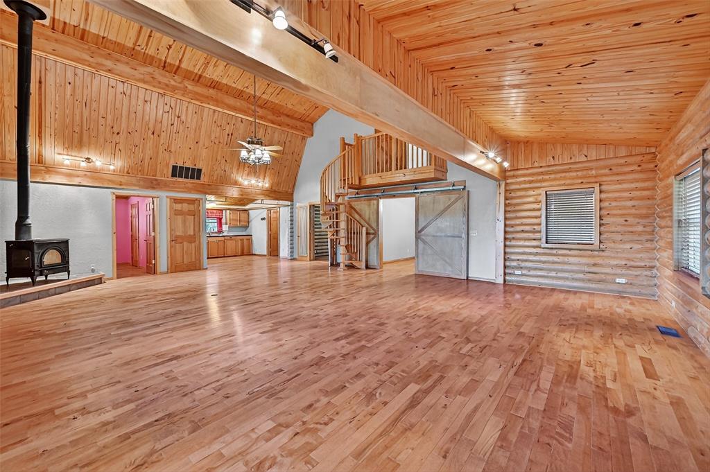 570 Ayres Road Bells, TX 75414 - Photo 10 of 39 Unfurnished living room with a wood stove, rustic walls, hardwood / wood-style flooring, wood ceiling, and high vaulted ceiling