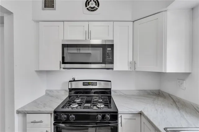 a kitchen with granite countertop white cabinets stove and microwave
