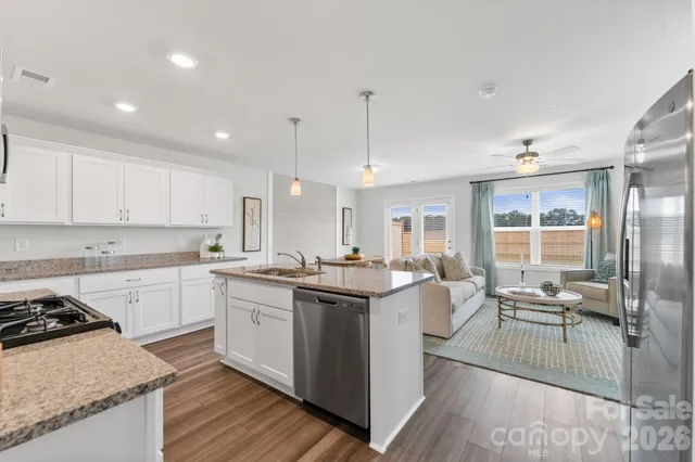 a kitchen with stainless steel appliances granite countertop a stove top oven a sink with white cabinets and wooden floor