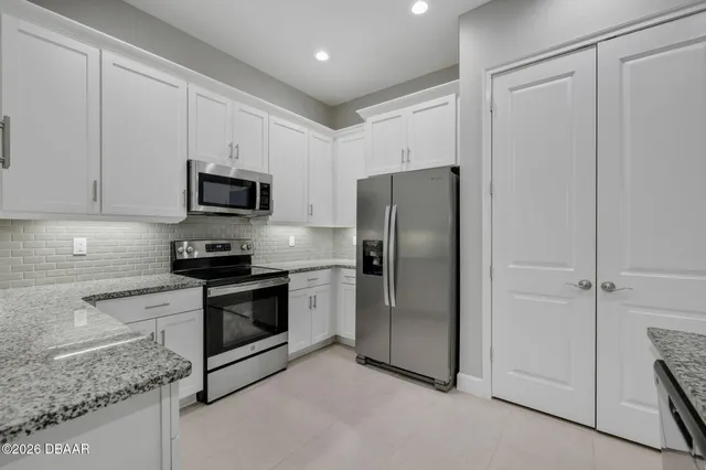 a kitchen with stainless steel appliances granite countertop a refrigerator a sink and white cabinets
