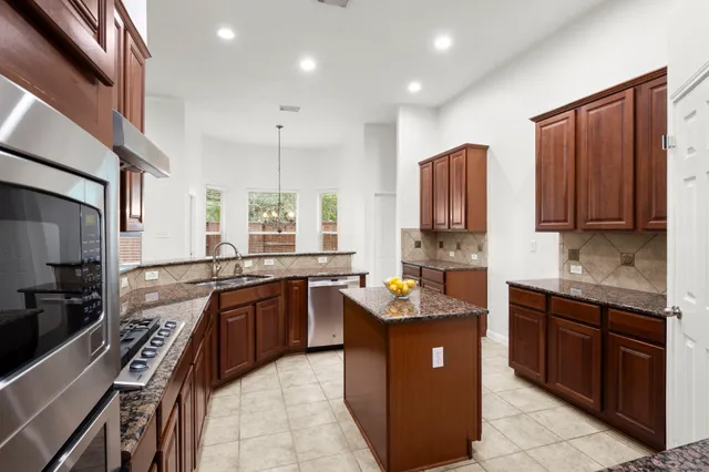 a kitchen with stainless steel appliances granite countertop wooden cabinets a sink dishwasher a stove and a refrigerator