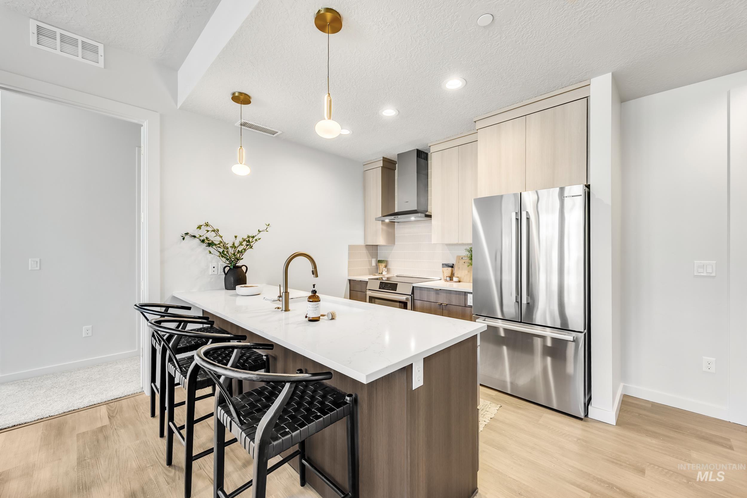 4340 East Haystack Street, Unit 104 Boise, ID 83716 - Photo 12 of 50 Kitchen featuring appliances with stainless steel finishes, pendant lighting, a kitchen bar, backsplash, and light stone countertops