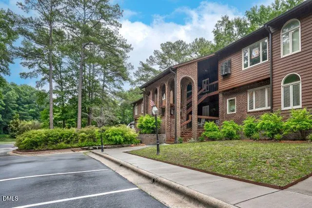a view of a brick house with a yard plants and large trees