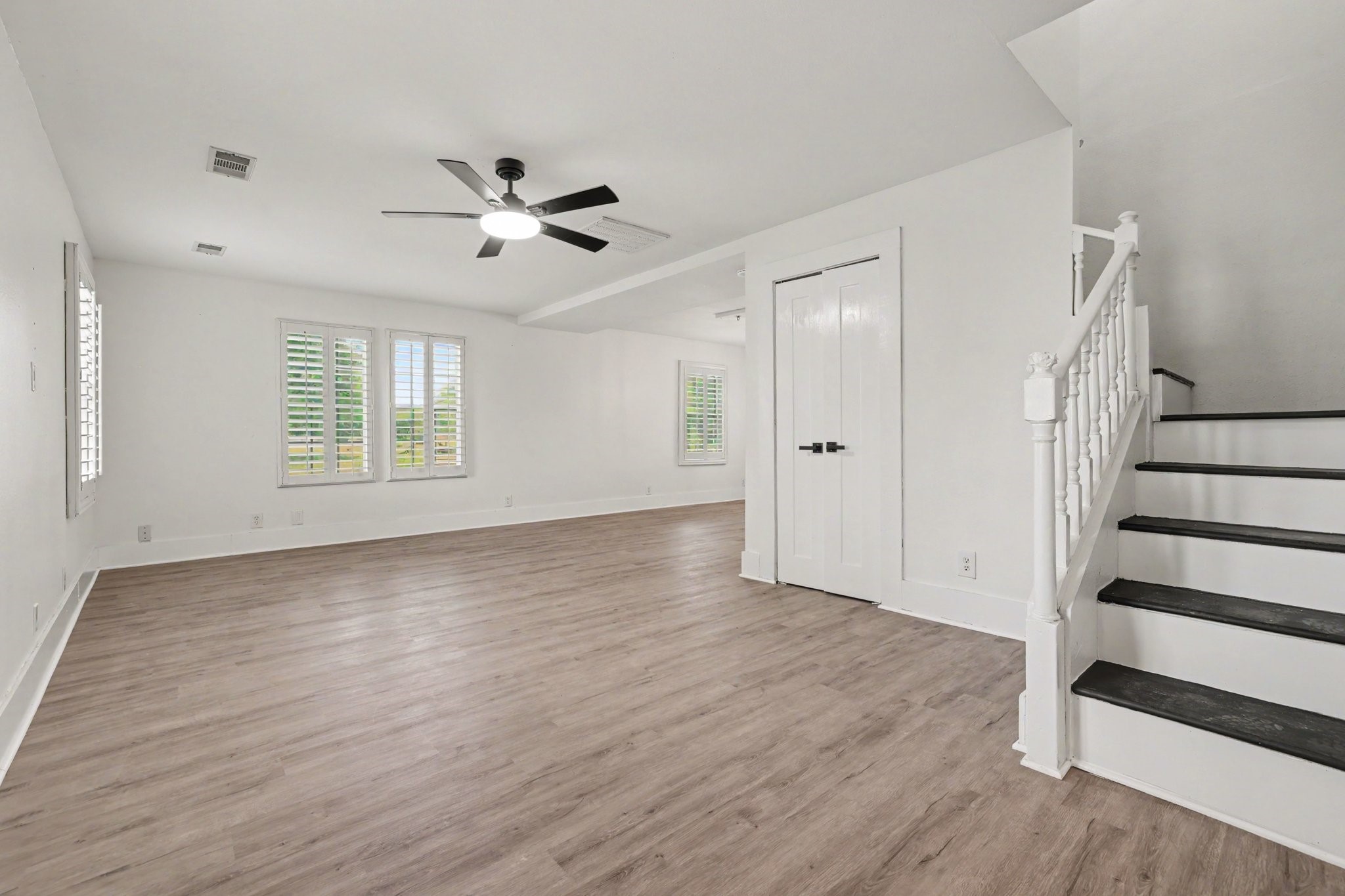 31730 Waller Tomball Road Waller, TX 77484 - Photo 18 of 50 Bright room with light vinyl flooring and large windows with shutters. It features a white and black staircase, offering a modern and open feel, perfect for a living area or family room.