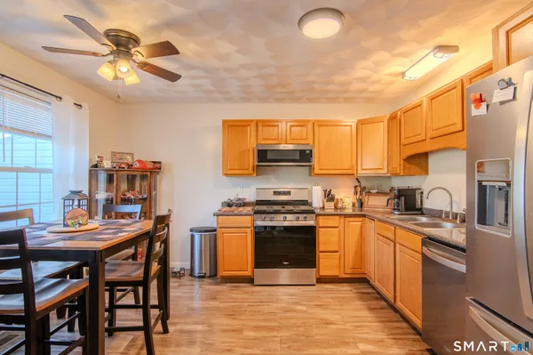 a kitchen with stainless steel appliances granite countertop a stove top oven a sink dishwasher a dining table and chairs with wooden floor